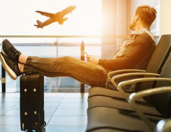 A man sits in an airport and looks out the window at a departing plane