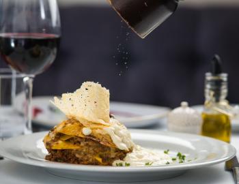 A plate of lasagna with a pepper grinder and a glass of wine