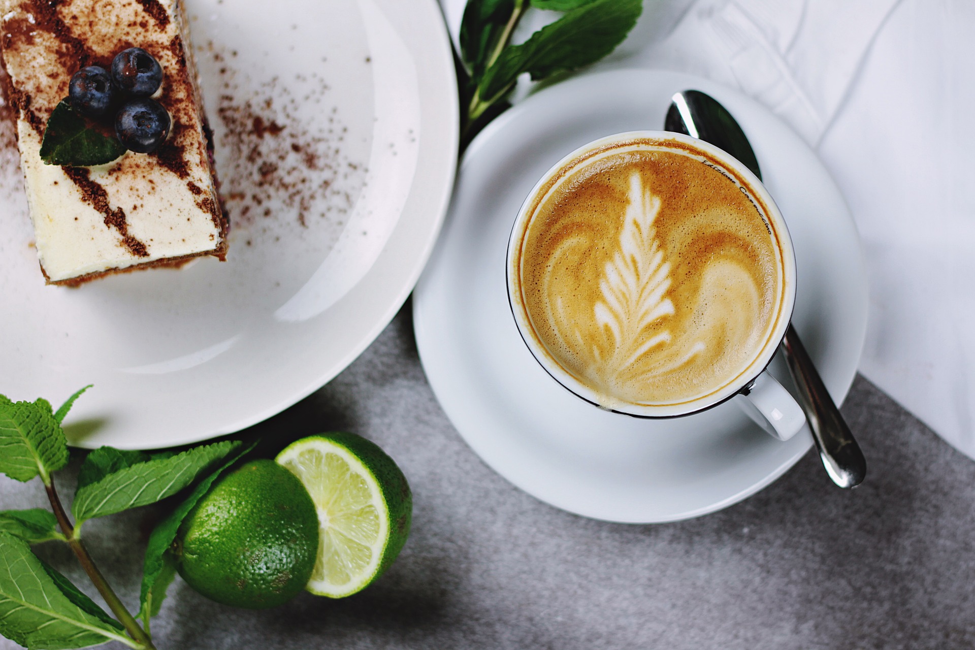 A cup of coffee on a table next to a book and a slice of cake