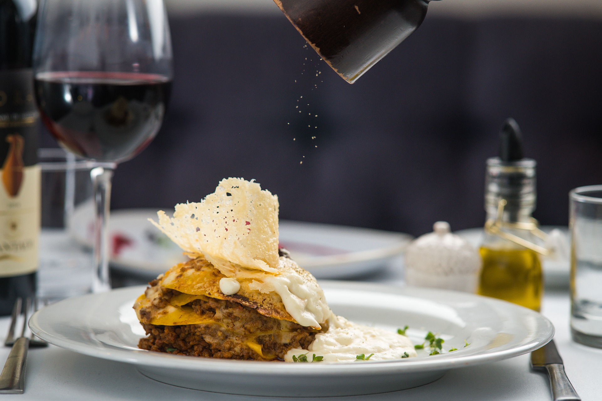 A plate of lasagna with a pepper grinder sprinkling pepper